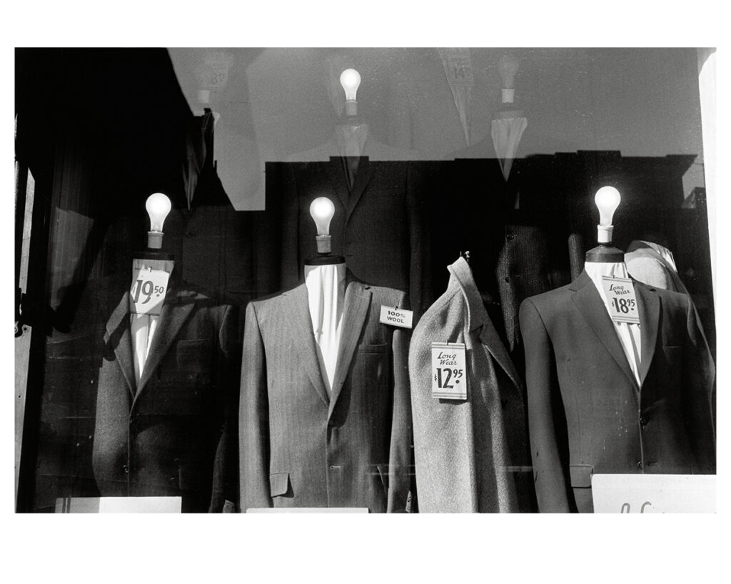 Headless suit mannequins with light bulbs for heads in a NYC store window, 1959.
